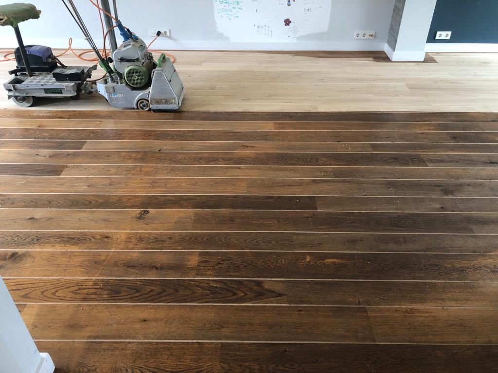 Donkere eiken vloer met kleurverschillen en slijtagesporen als nieuw en lichter na schuren van de vloer in Rosmalen.jpg