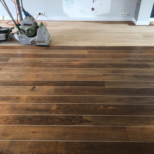 Donkere eiken vloer met kleurverschillen en slijtagesporen als nieuw en lichter na schuren van de vloer in Rosmalen.jpg